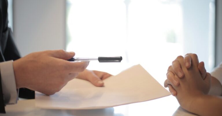 person handing a pen to sign contract