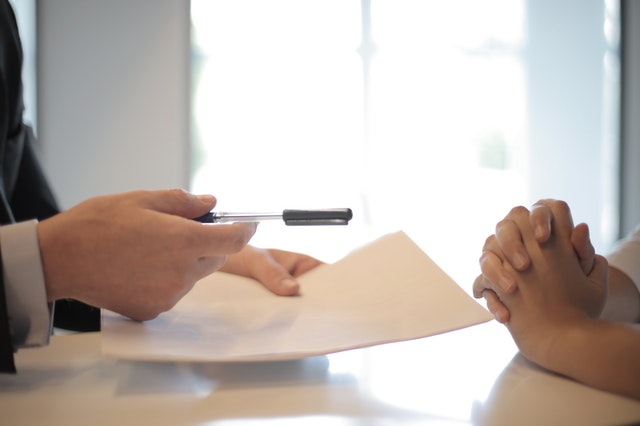 person handing a pen to sign contract